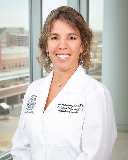 Brunette woman in white coat standing in front of a window