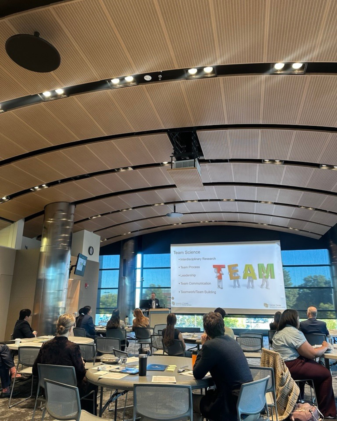 Room of attendees being presented to with a projector screen