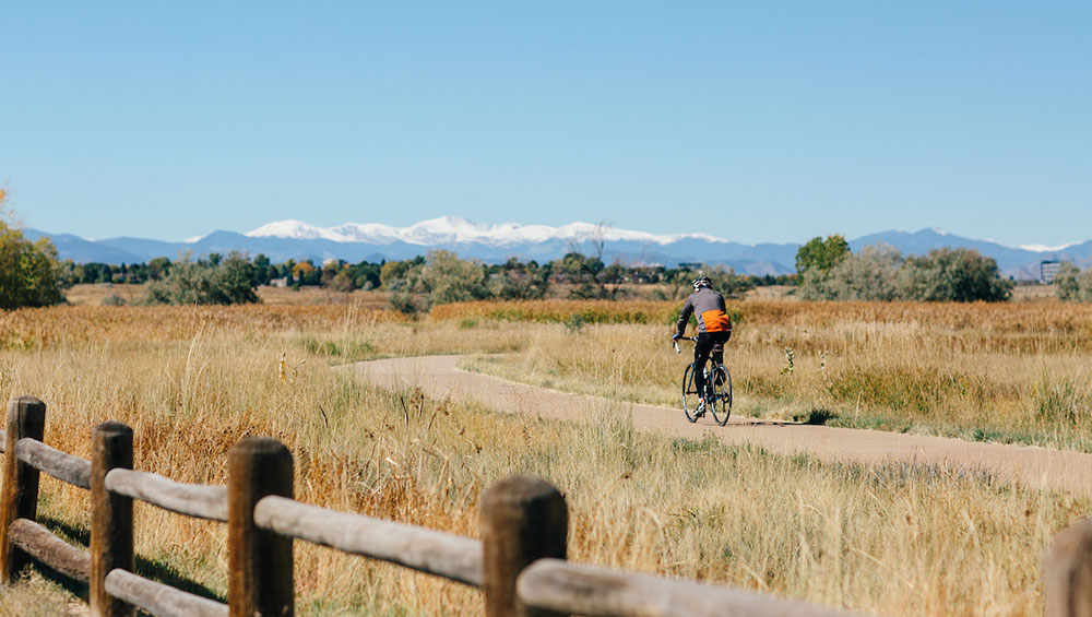 A person riding a bike through Cherry Creek State Park with mountains in the background