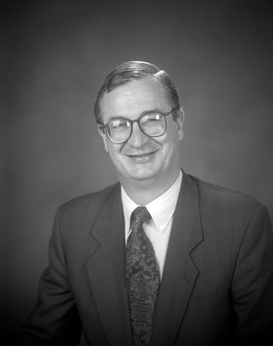 Dr. Norris black and white portrait from 1996, wearing a black suit and tie, smiling