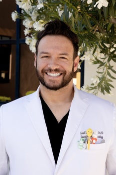 Israel Andrews MD wearing a white coat and smiling on a sunny day