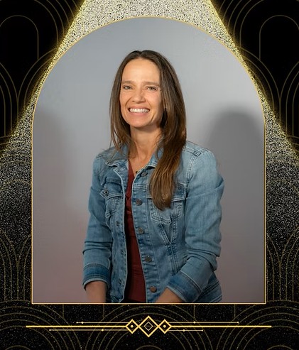 Aimee Bernard, PhD's photo framed in gold with a black background that has a spotlight shining behind the photo and a gold embellishment below the photo.