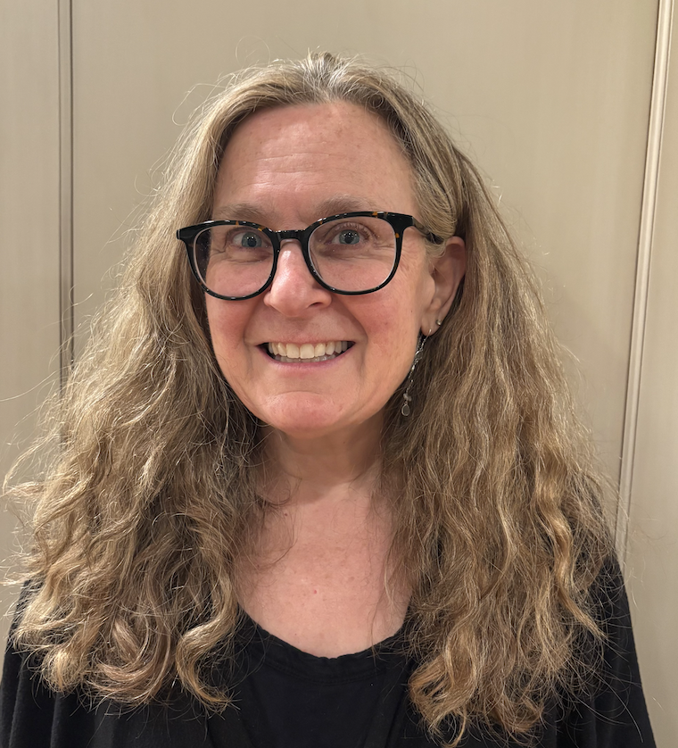 female with blonde wavy hair, smiling, with black glasses on and a black shirt