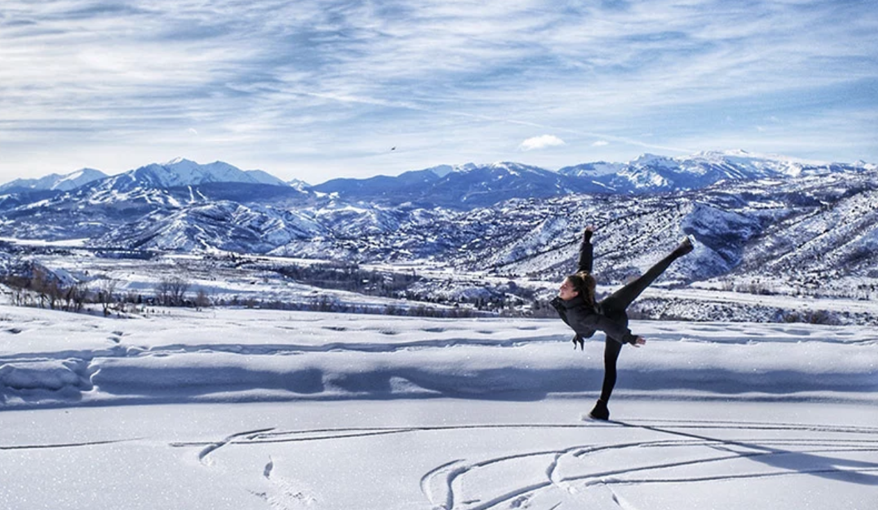 Figure skater Sari Behr skating on the ice in front of the mountains.