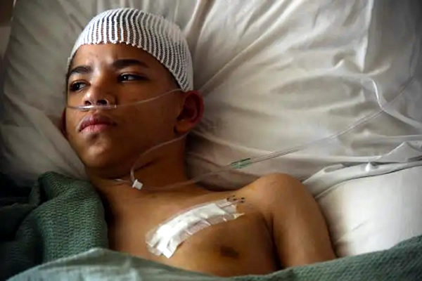 A young patient rests in his hospital bed the day after the second part of deep brain stimulation surgery