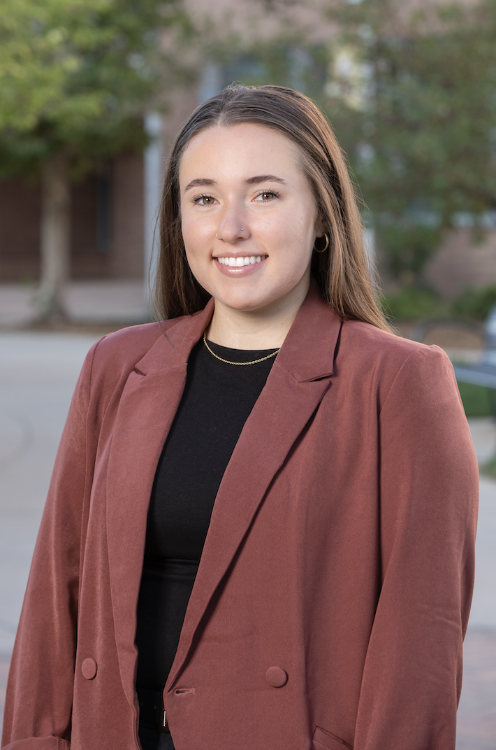 female wearing a salmon colored blazer and black shirt smiling and posing for a headshot