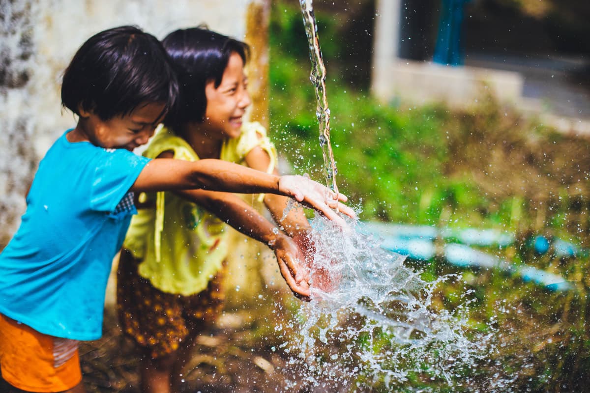 Two children putting hands under clean water