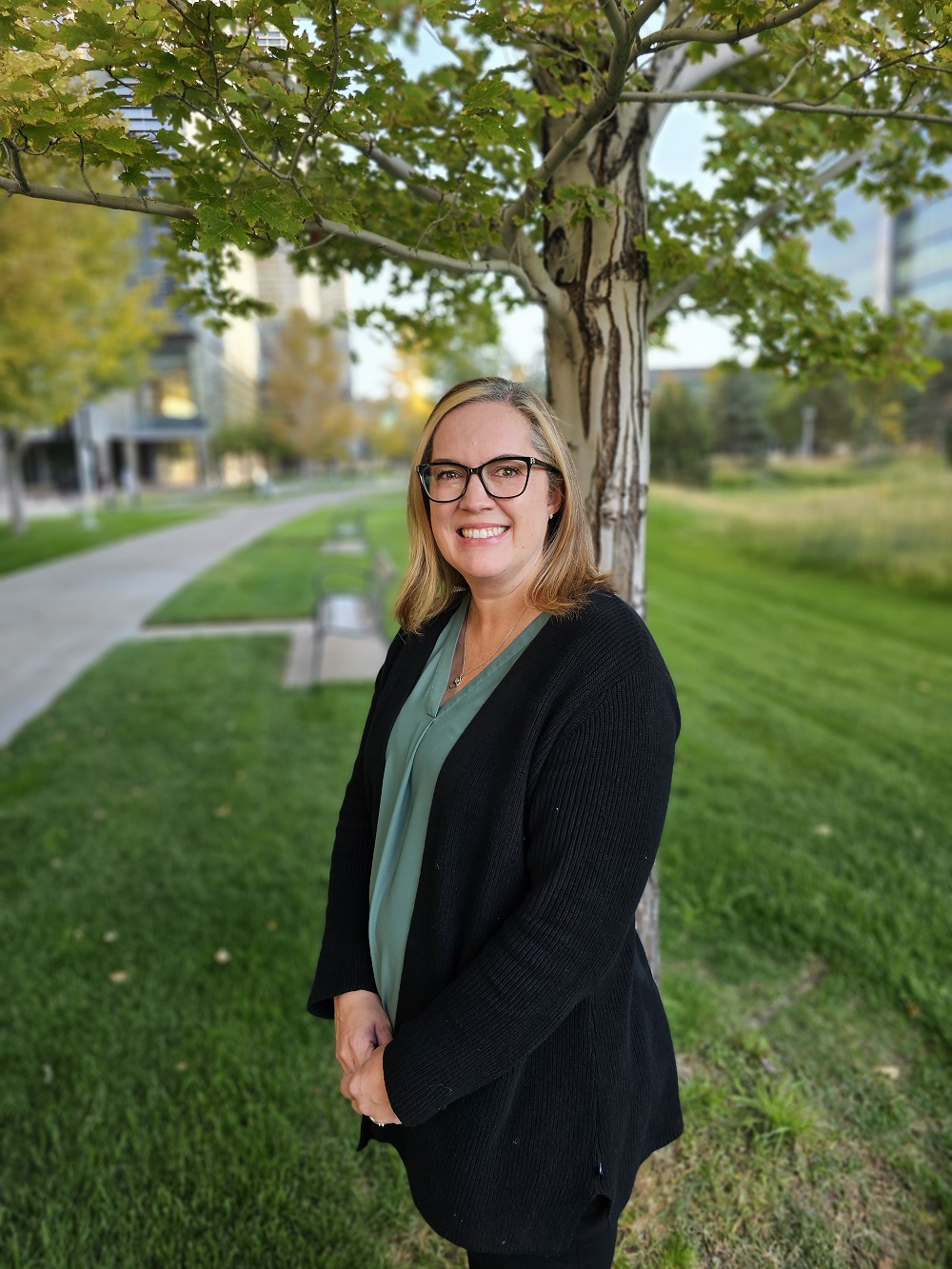 Headshot of Kelly Batory with campus buildings and trees in the background.