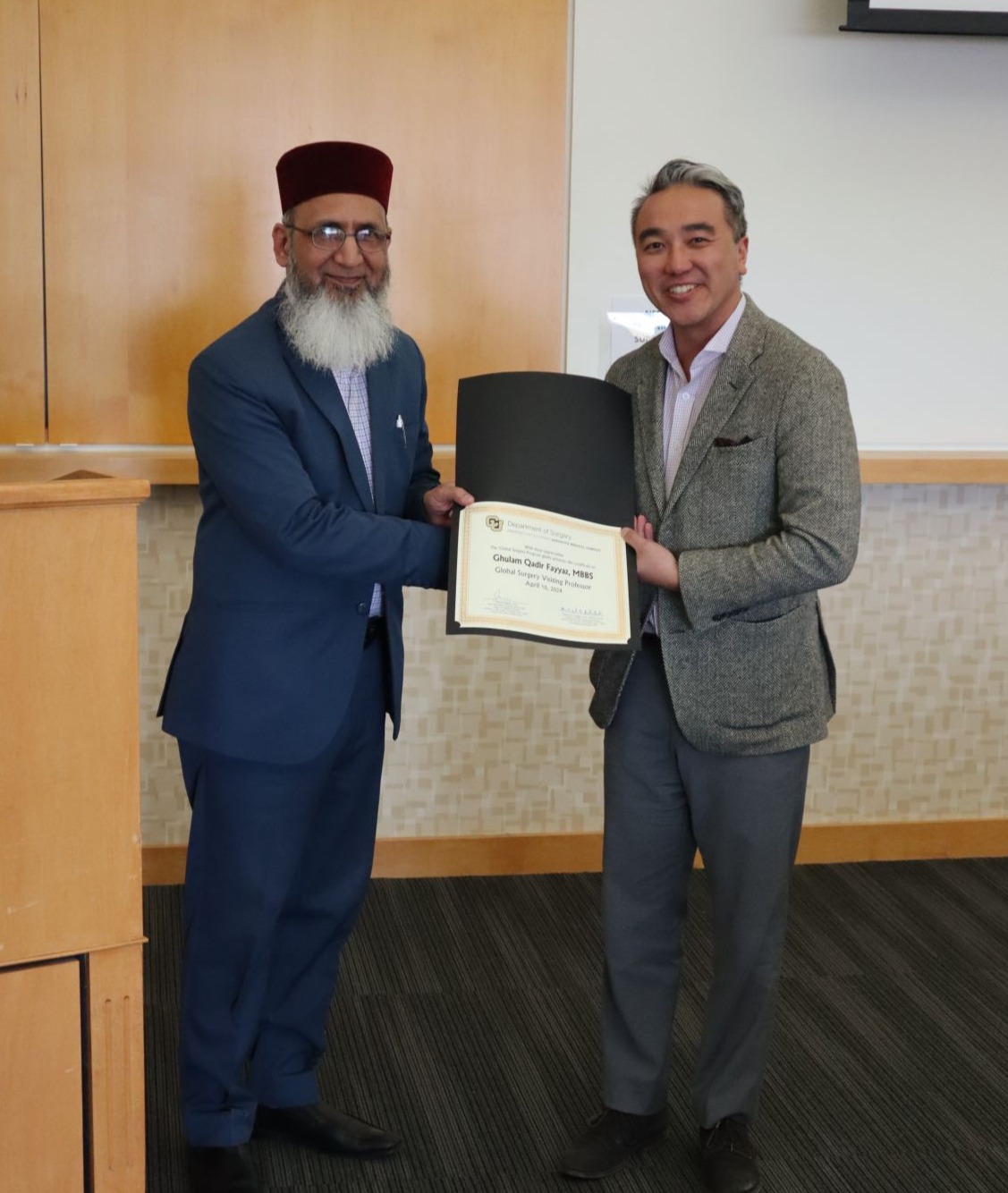 Drs. Phuong Nguyen and Ghulam Qadir Fayyaz shake hands and hold certificate in conference room