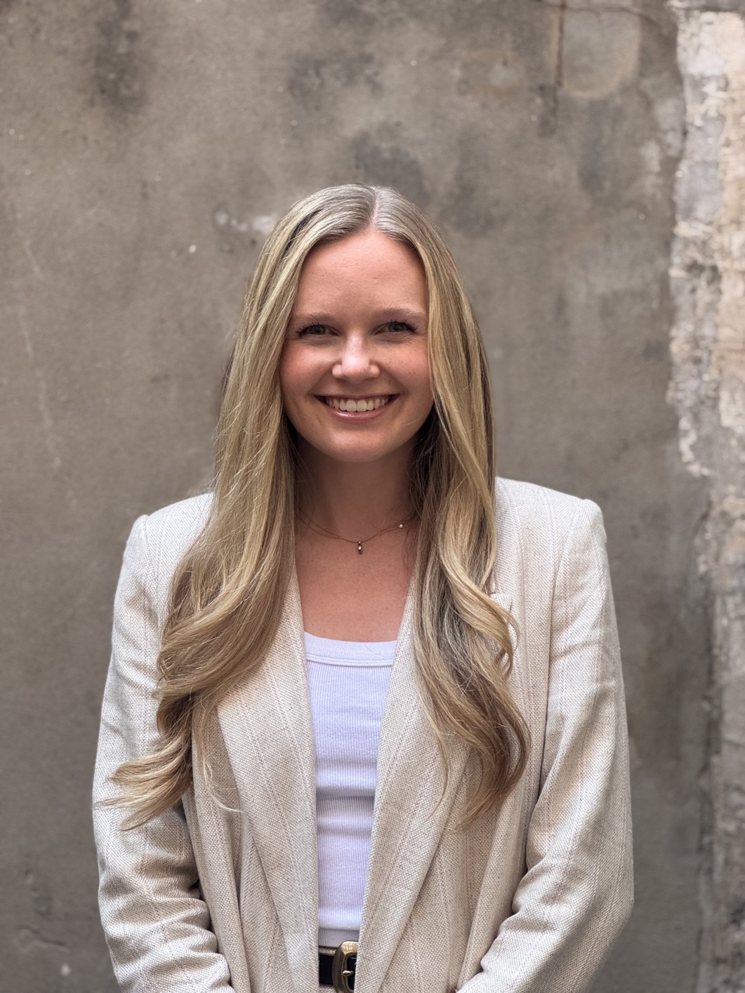 Headshot of woman in tan blazer in front a blank background.