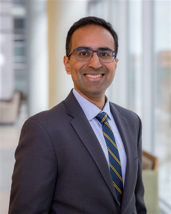 Professional Headshot of man in tie. Background is a blurred hallway.