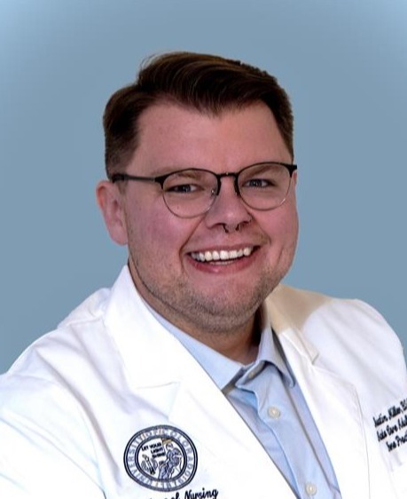 Professional headshot of man with short hair in white medical coat in front of a plain blue background.
