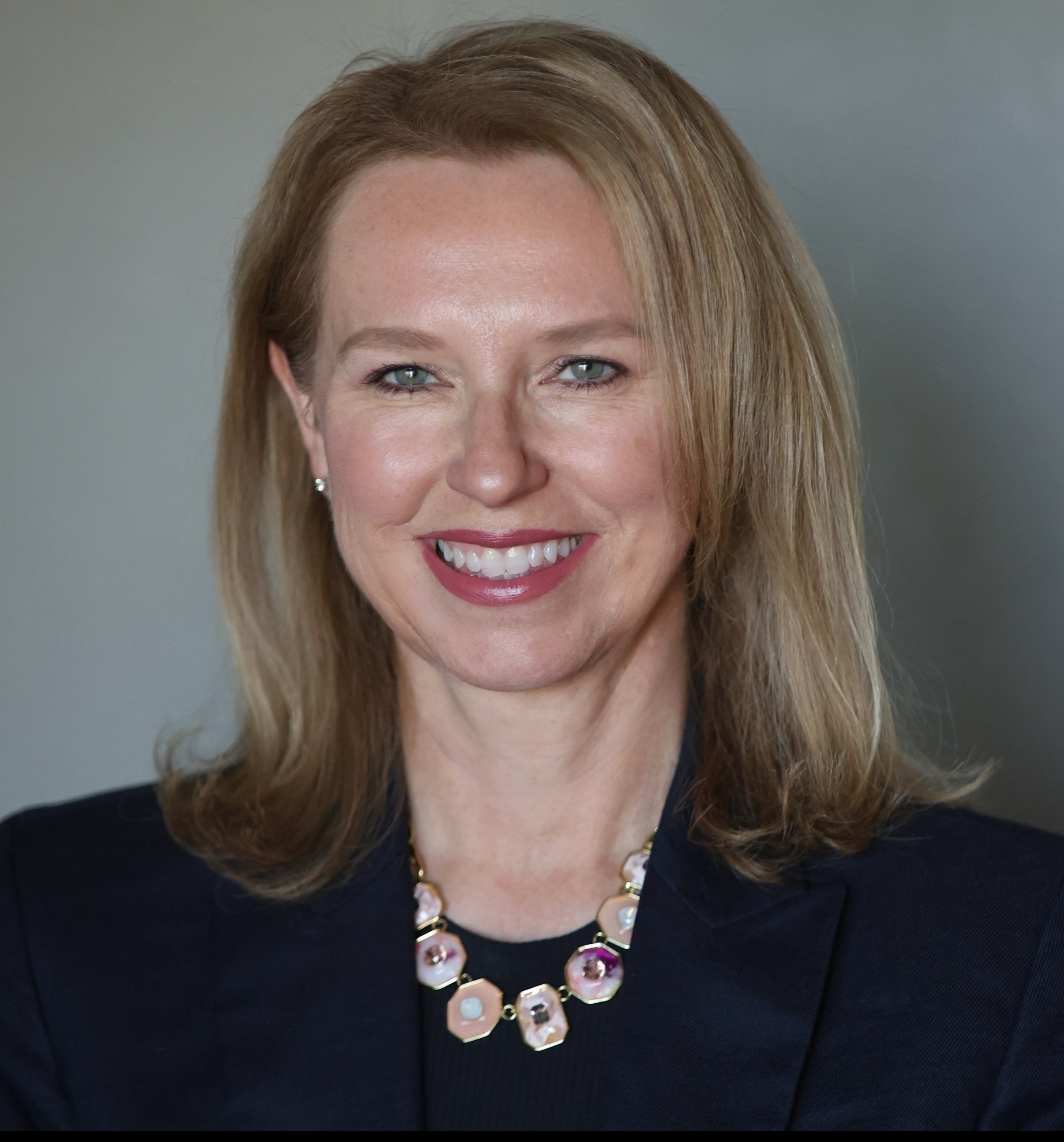 Headshot of woman in navy blazer with blank background.