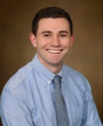 Professional headshot of man in tie, with blank background.