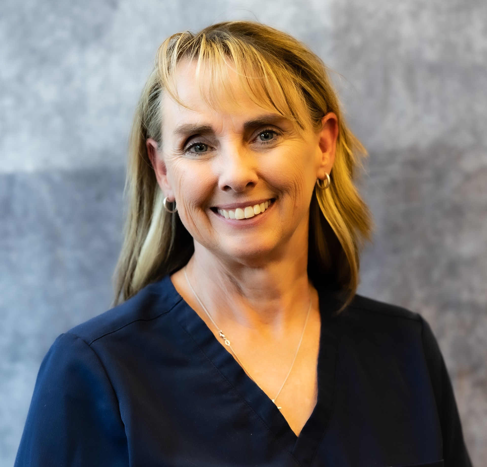 Professional headshot of woman in scrubs. Background is blank.
