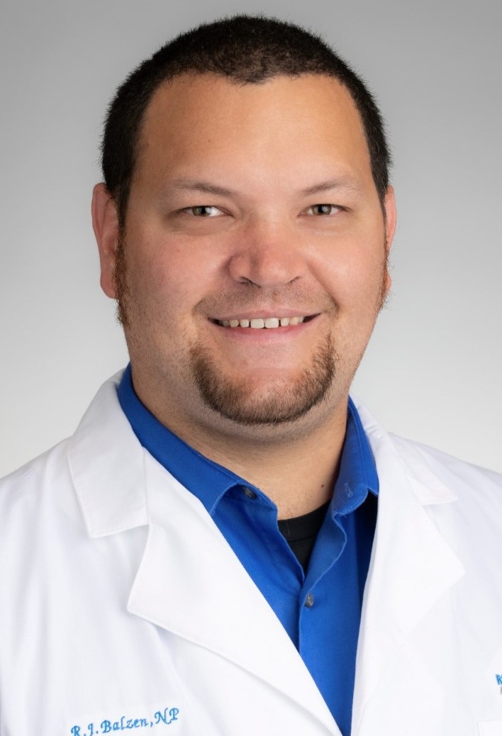 Headshot of man in collared shirt and white coat. Background is blank.