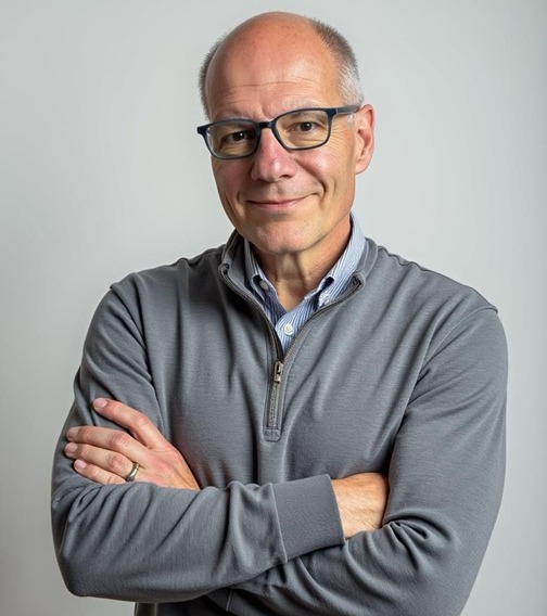 Photograph of  a man from waist up. Arms are crossed