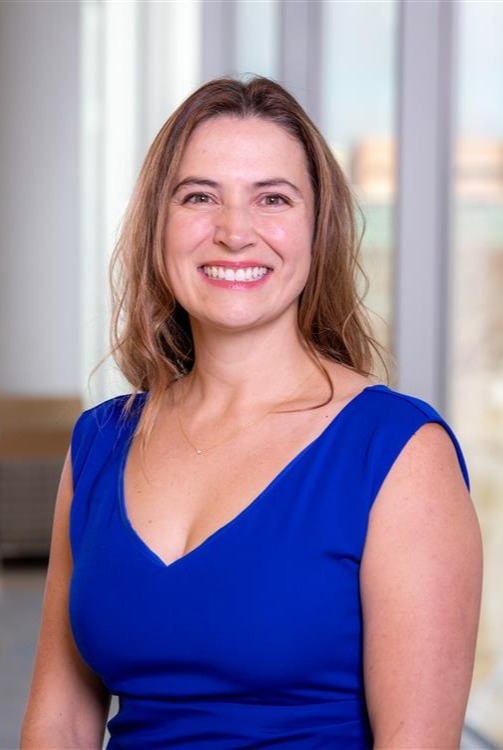 Professional headshot of woman. Background is blurred hallway.