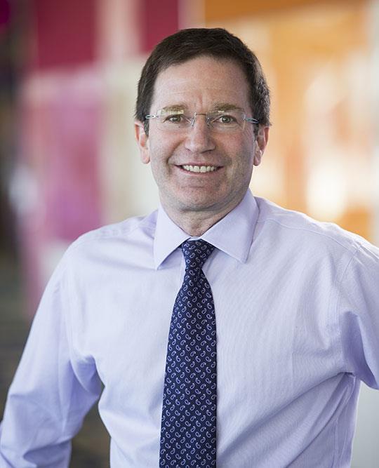 Professional headshot of man in shirt and tie. Background is blurred.