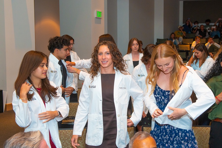 CU PT Class of 2028 students putting on their white coats.