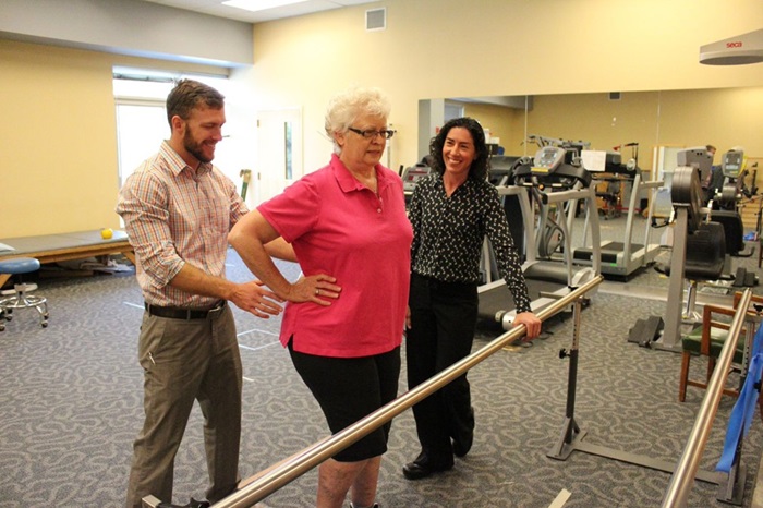 A woman in a lab being assisted by 2 physical therapists.