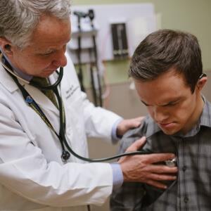 Dr. Barry Martin listens with a stethoscope to a young man with Down syndrome