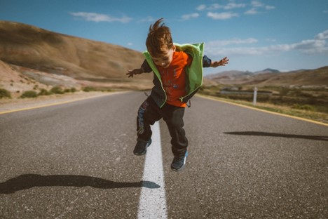 Young boy jumping in the middle of a road in the mountains.